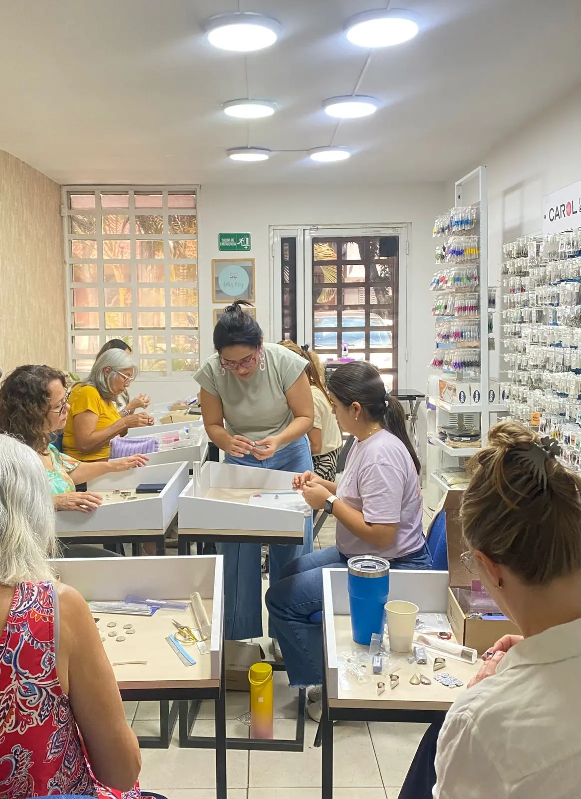 Un grupo de mujeres modelando arcilla polimérica en mesas de trabajo durante una clase presencial en una tienda Carol